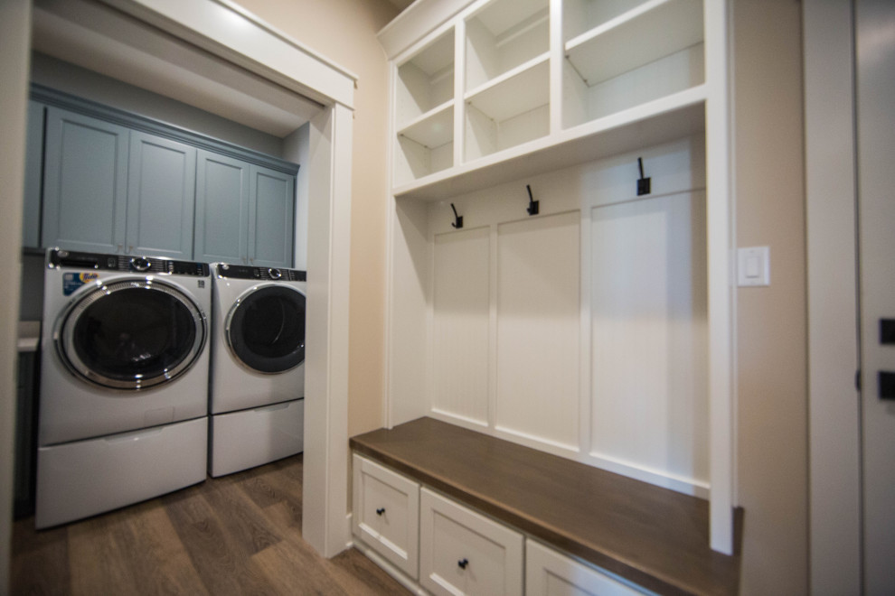 Foto di una sala lavanderia chic di medie dimensioni con ante con riquadro incassato, ante blu, pareti beige, pavimento in laminato, lavatrice e asciugatrice affiancate e pavimento marrone