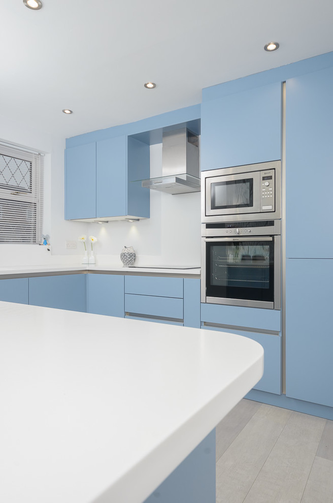 Mid-sized modern l-shaped eat-in kitchen in Other with an integrated sink, flat-panel cabinets, blue cabinets, solid surface benchtops, white splashback, panelled appliances, linoleum floors and a peninsula.