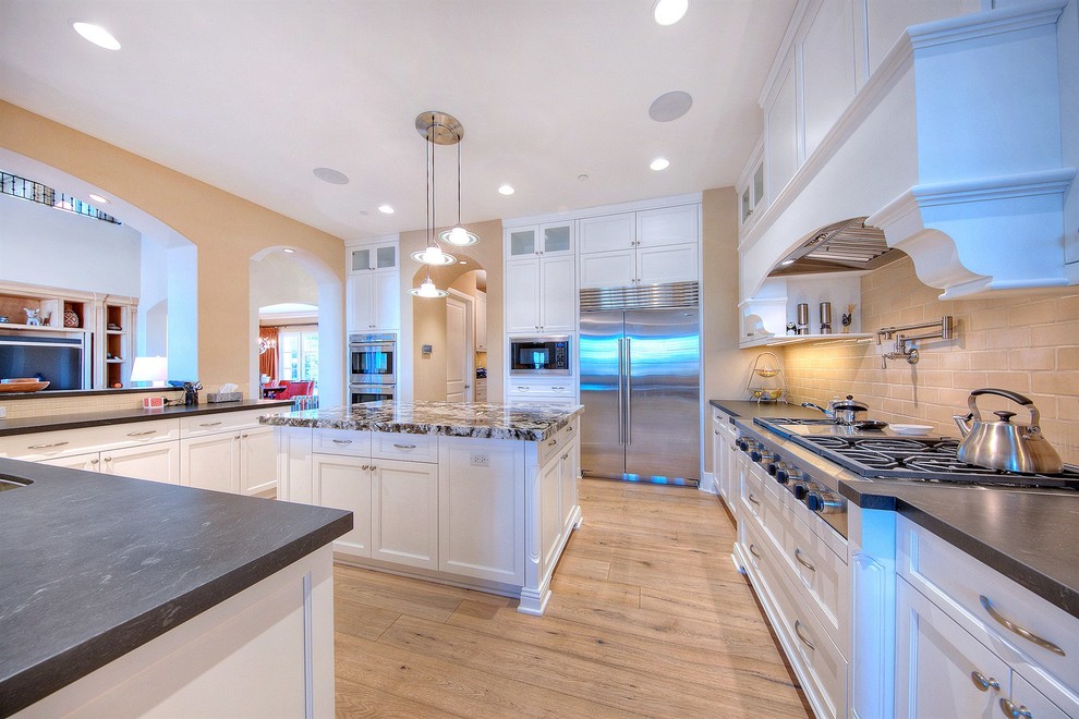 Inspiration for a large mediterranean light wood floor kitchen remodel in Phoenix with white cabinets, stainless steel appliances and an island