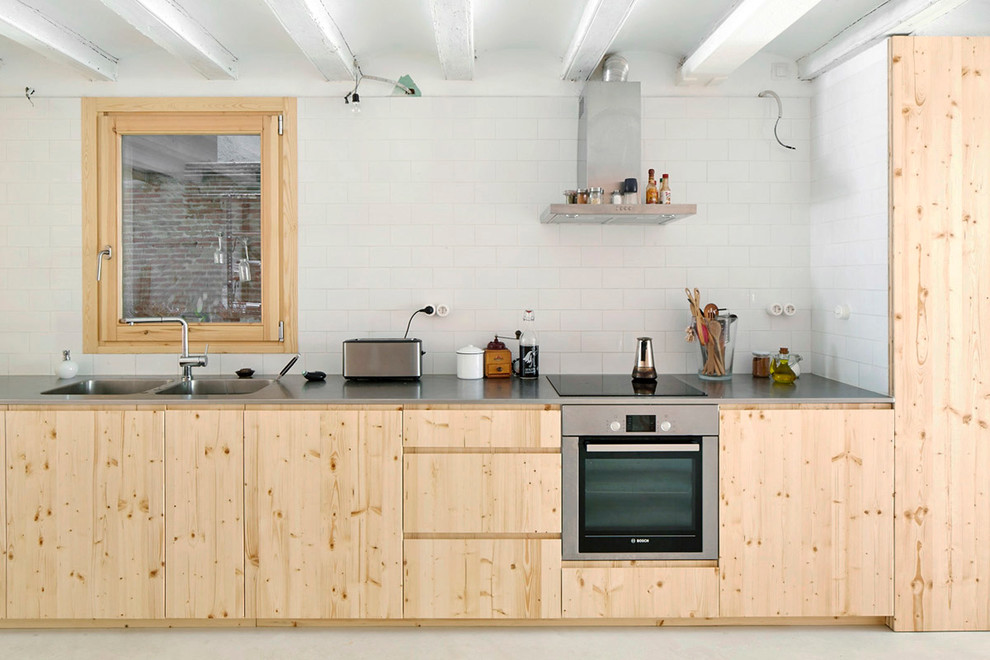 This is an example of a mid-sized scandinavian single-wall kitchen in Barcelona with a double-bowl sink, flat-panel cabinets, light wood cabinets, stainless steel benchtops, white splashback, subway tile splashback, stainless steel appliances and no island.