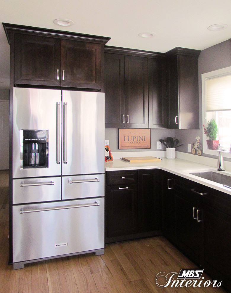 Large transitional l-shaped light wood floor eat-in kitchen photo with an undermount sink, recessed-panel cabinets, dark wood cabinets, quartz countertops, stainless steel appliances and an island