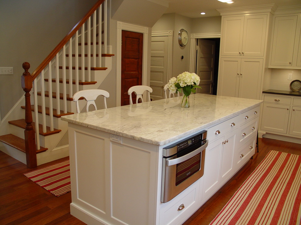 Example of a transitional enclosed kitchen design in Boston with a farmhouse sink, recessed-panel cabinets, white cabinets, granite countertops, white backsplash, subway tile backsplash, stainless steel appliances and an island