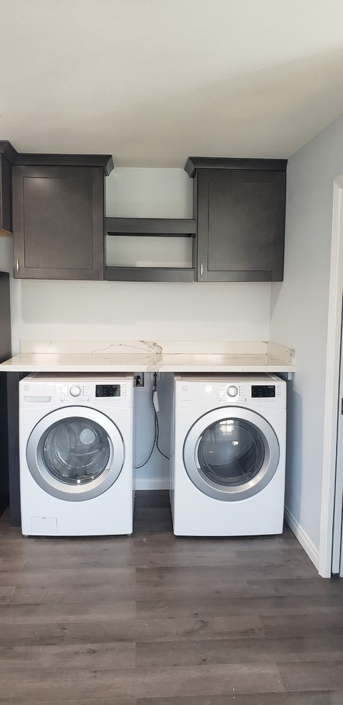 Photo of a modern single-wall utility room in Orange County with shaker cabinets, black cabinets, quartzite benchtops, blue walls and a side-by-side washer and dryer.
