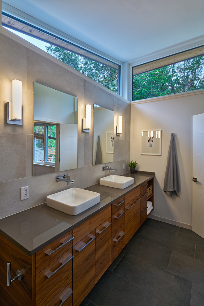 This is an example of a contemporary bathroom in Grand Rapids with flat-panel cabinets, medium wood cabinets, gray tile, white walls, a vessel sink, grey floor and grey benchtops.