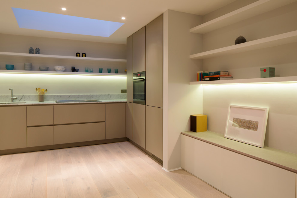 This is an example of a small scandinavian l-shaped open plan kitchen in London with flat-panel cabinets, beige cabinets, marble benchtops, light hardwood floors, no island and white benchtop.
