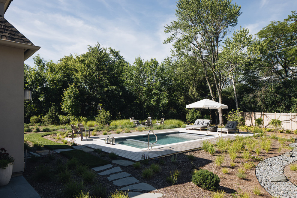Diseño de piscina grande rectangular en patio trasero con paisajismo de piscina y adoquines de hormigón