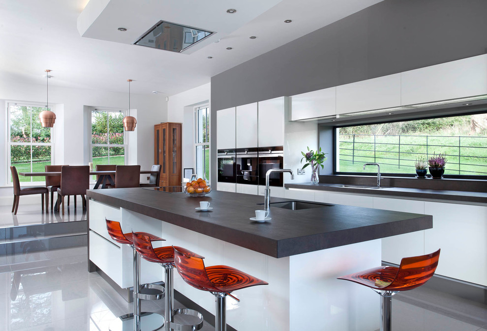 Photo of a large contemporary single-wall open plan kitchen in Belfast with an integrated sink, flat-panel cabinets, white cabinets, quartz benchtops, grey splashback, stone slab splashback, stainless steel appliances, porcelain floors and with island.