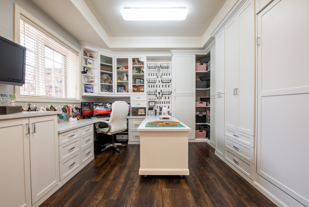 Design ideas for a mid-sized arts and crafts craft room in Denver with white walls, dark hardwood floors, a built-in desk and brown floor.