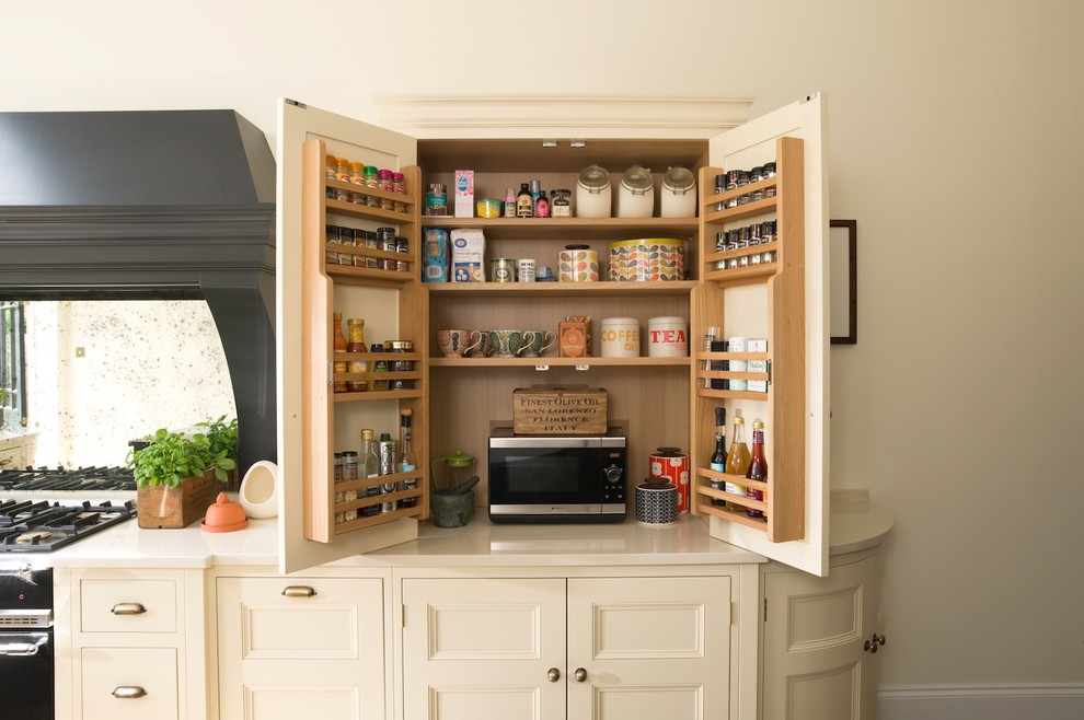 This is an example of a mid-sized traditional kitchen pantry in Kent with recessed-panel cabinets, quartzite benchtops, mirror splashback, dark hardwood floors and black appliances.