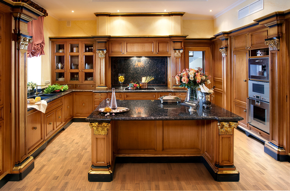 Photo of a large traditional u-shaped kitchen in Milan with a double-bowl sink, recessed-panel cabinets, medium wood cabinets, marble benchtops, stainless steel appliances, light hardwood floors and with island.