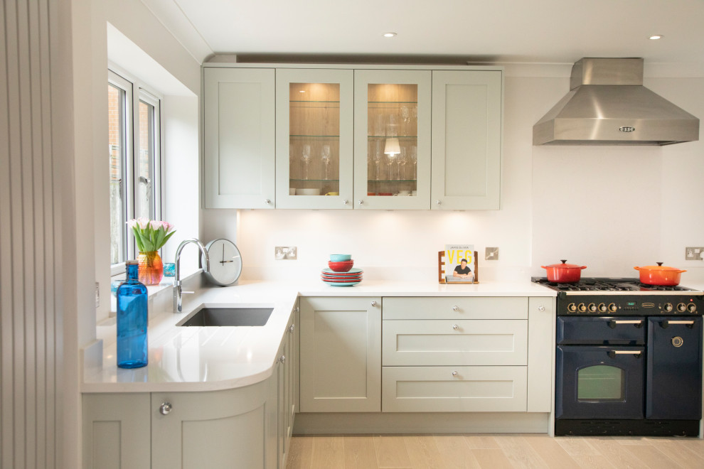 Design ideas for a mid-sized transitional l-shaped kitchen in Berkshire with an undermount sink, shaker cabinets, green cabinets, coloured appliances, beige floor and white benchtop.