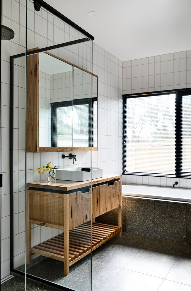 Design ideas for a mid-sized contemporary master bathroom in Other with furniture-like cabinets, light wood cabinets, a drop-in tub, a curbless shower, white tile, subway tile, white walls, terrazzo floors, a vessel sink, wood benchtops, grey floor and a hinged shower door.