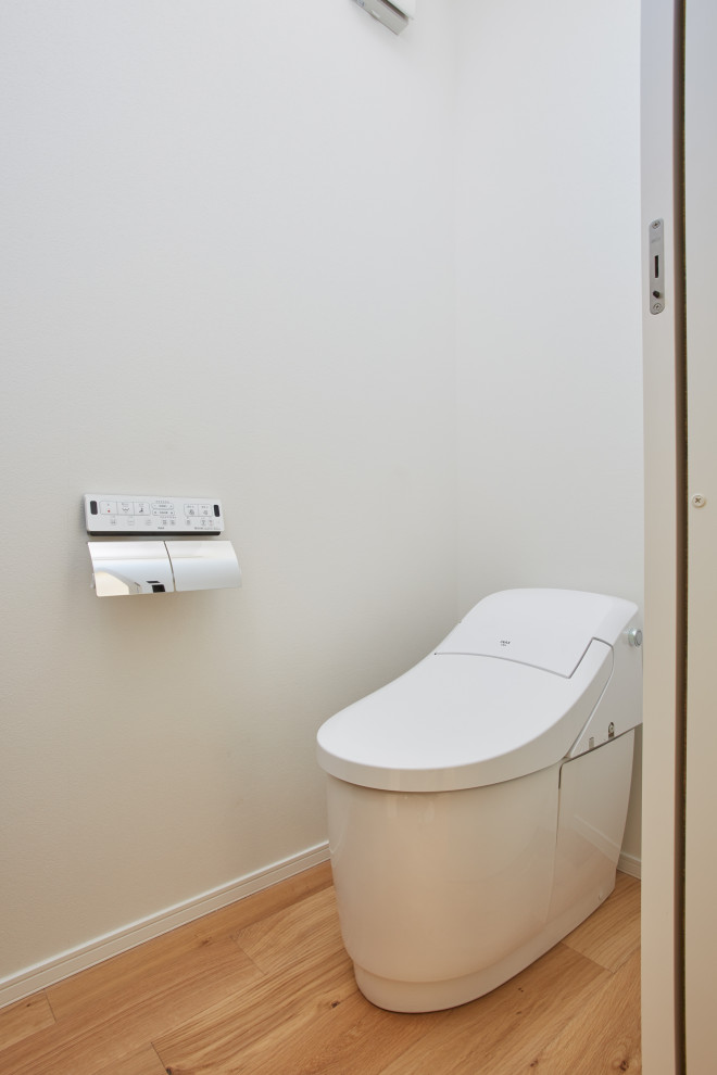 This is an example of a small powder room in Tokyo with a one-piece toilet, white tile, white walls, medium hardwood floors and wallpaper.