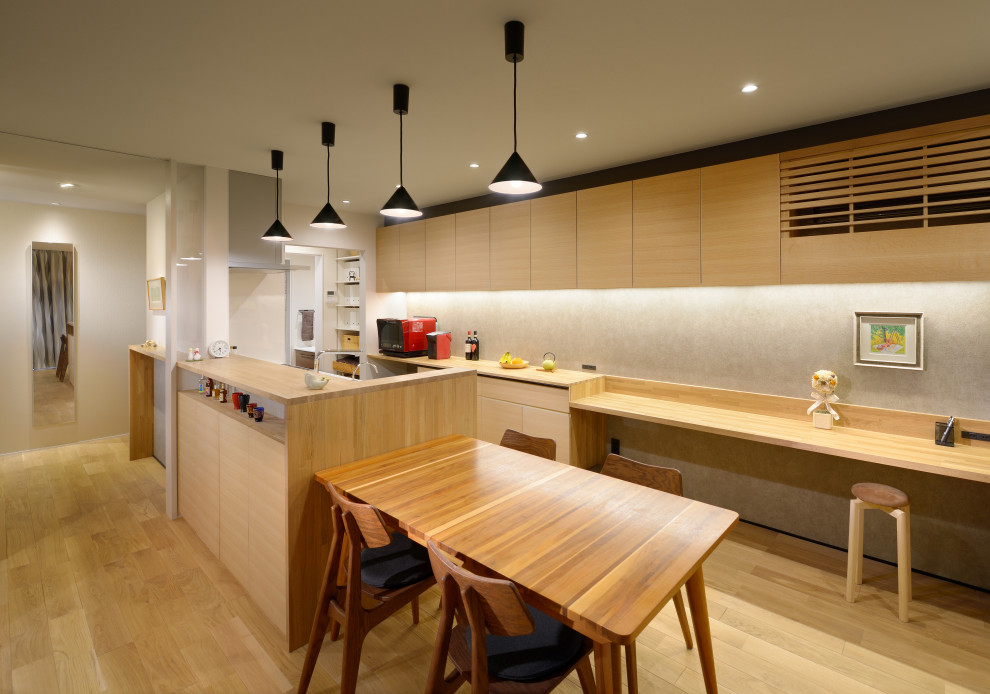 Design ideas for a mid-sized asian galley eat-in kitchen with flat-panel cabinets, light wood cabinets, wood benchtops, grey splashback, panelled appliances, light hardwood floors, no island, beige floor and beige benchtop.