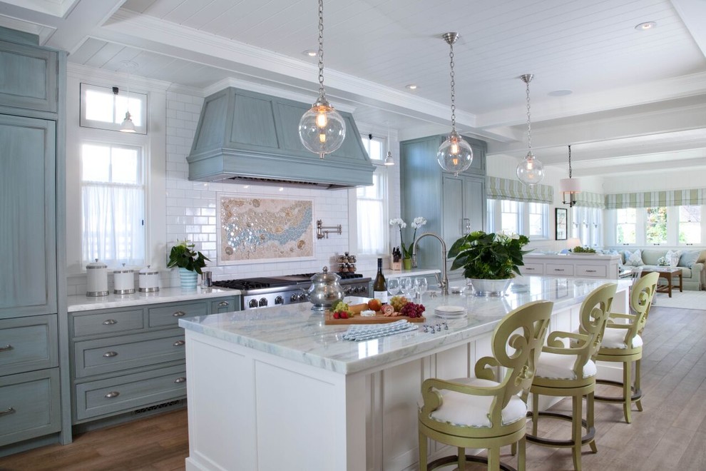 Inspiration for a large beach style l-shaped eat-in kitchen in San Diego with a farmhouse sink, shaker cabinets, blue cabinets, marble benchtops, white splashback, subway tile splashback, stainless steel appliances, medium hardwood floors, with island and brown floor.