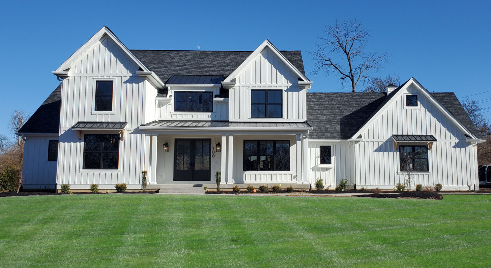 Foto della villa bianca country a due piani con rivestimento con lastre in cemento, tetto a capanna, copertura mista, tetto grigio e pannelli e listelle di legno
