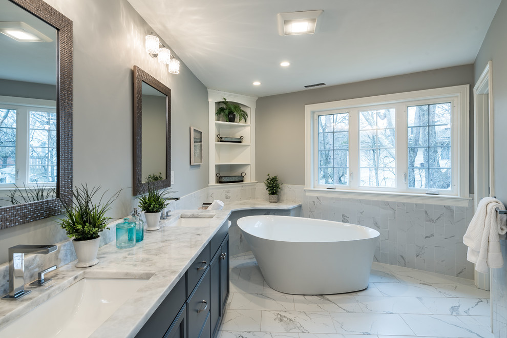 This is an example of a large contemporary master bathroom in Boston with recessed-panel cabinets, grey cabinets, a freestanding tub, marble, grey walls, marble floors, an undermount sink, marble benchtops, white floor and white benchtops.