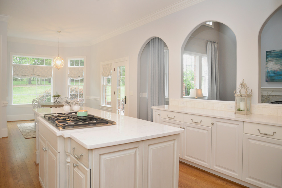 Transitional light wood floor kitchen photo with white cabinets, beige backsplash, stainless steel appliances and an island