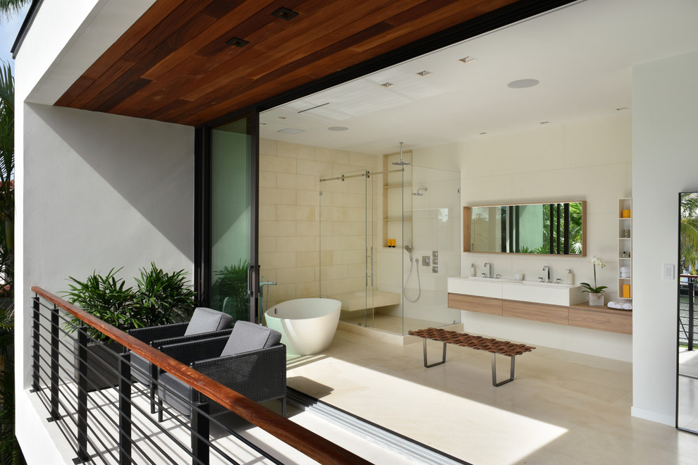 This is an example of a contemporary master bathroom in Miami with flat-panel cabinets, medium wood cabinets, a freestanding tub, a corner shower, beige tile, beige floor and a sliding shower screen.