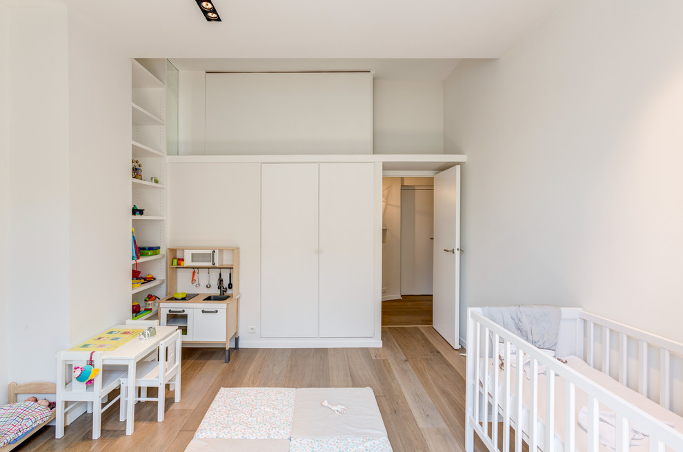 Mid-sized scandinavian gender-neutral nursery in Paris with white walls, light hardwood floors and beige floor.