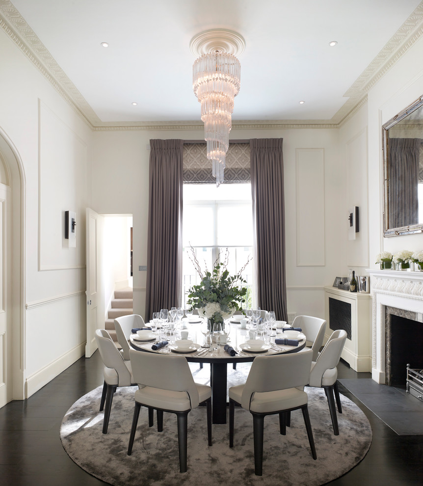 This is an example of a traditional dining room in London with white walls, dark hardwood floors, a standard fireplace and a stone fireplace surround.