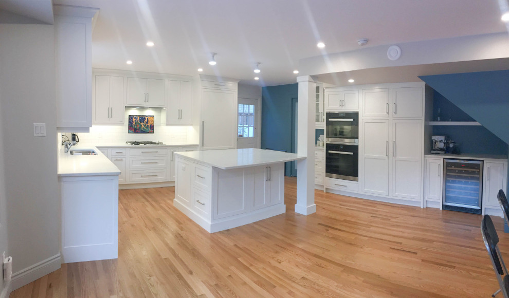 Large transitional u-shaped light wood floor and beige floor eat-in kitchen photo with a double-bowl sink, shaker cabinets, white cabinets, quartzite countertops, white backsplash, subway tile backsplash, stainless steel appliances, an island and white countertops