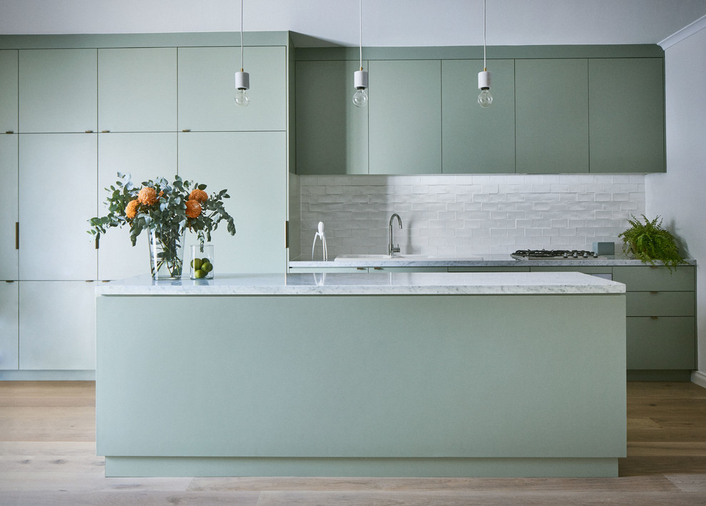 Mid-sized contemporary galley kitchen in Melbourne with a double-bowl sink, flat-panel cabinets, green cabinets, marble benchtops, white splashback, ceramic splashback, light hardwood floors, with island, brown floor, white benchtop and panelled appliances.