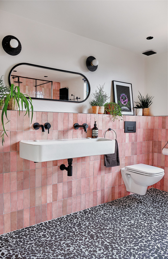 Mid-sized contemporary kids bathroom in London with black cabinets, an open shower, a wall-mount toilet, pink tile, ceramic tile, white walls, terrazzo floors, a trough sink, black floor, an open shower, a niche, a single vanity and a floating vanity.