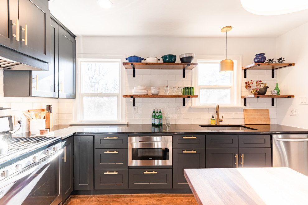 This is an example of a small contemporary galley separate kitchen in Denver with an undermount sink, shaker cabinets, black cabinets, quartzite benchtops, white splashback, ceramic splashback, stainless steel appliances, dark hardwood floors, a peninsula, brown floor and black benchtop.