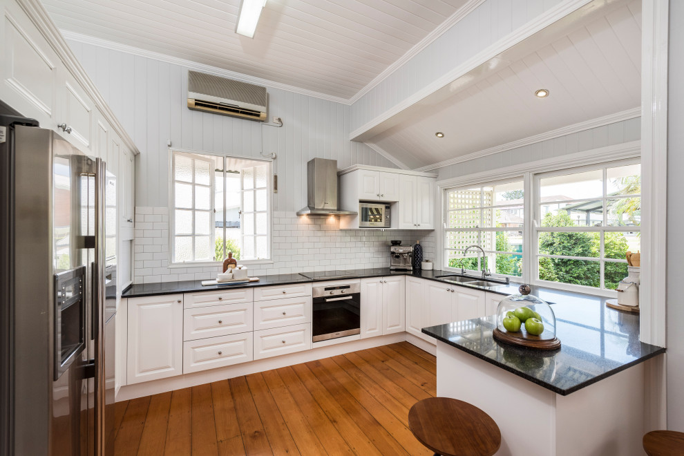 Design ideas for a mid-sized u-shaped eat-in kitchen in Brisbane with white cabinets, laminate benchtops, white splashback, panelled appliances, brown floor, black benchtop and timber.