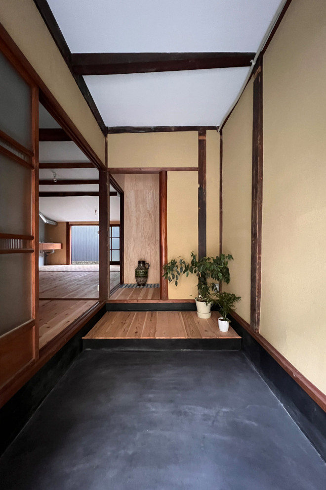 Eingang mit beiger Wandfarbe, Betonboden, Schiebetür, dunkler Holzhaustür, schwarzem Boden und freigelegten Dachbalken in Kyoto