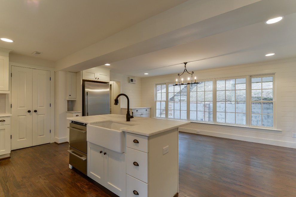 Example of a mid-sized transitional u-shaped dark wood floor eat-in kitchen design in Birmingham with a farmhouse sink, shaker cabinets, white cabinets, white backsplash, stainless steel appliances, an island, marble countertops and porcelain backsplash