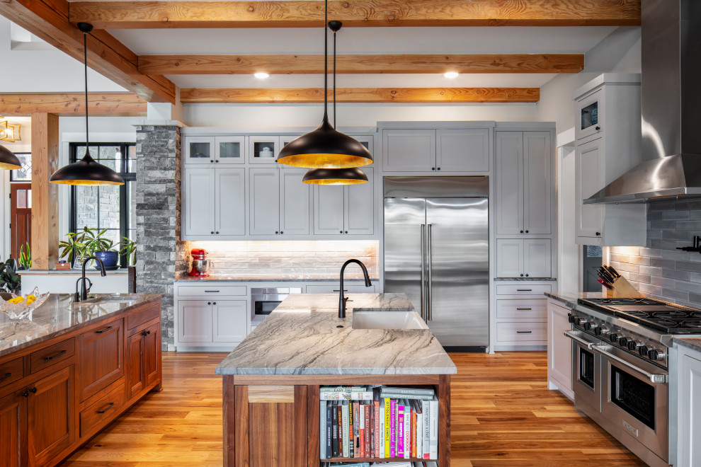 Design ideas for an expansive country open plan kitchen in Austin with a farmhouse sink, shaker cabinets, grey cabinets, marble benchtops, grey splashback, stone tile splashback, stainless steel appliances, medium hardwood floors, multiple islands, brown floor, grey benchtop and exposed beam.
