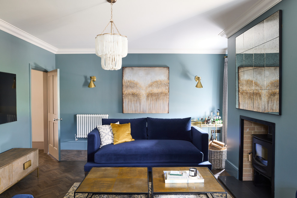 エセックスにある高級な広いコンテンポラリースタイルのおしゃれなリビング (青い壁、濃色無垢フローリング、薪ストーブ、漆喰の暖炉まわり、壁掛け型テレビ、茶色い床) の写真