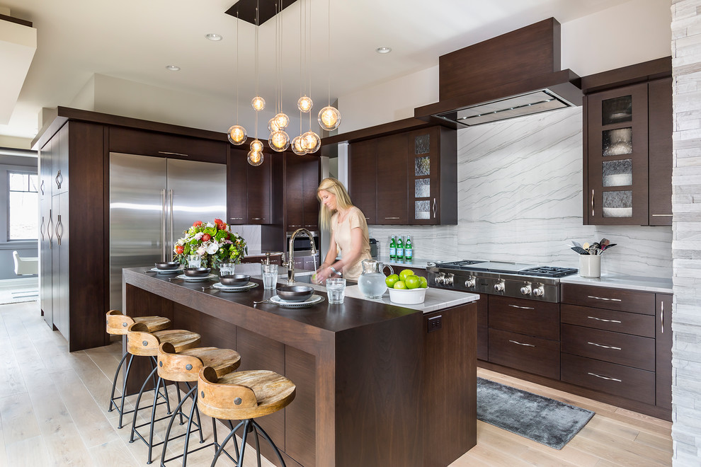 Example of a mountain style l-shaped light wood floor and beige floor kitchen design in Minneapolis with flat-panel cabinets, dark wood cabinets, multicolored backsplash, stone slab backsplash, stainless steel appliances, an island and gray countertops