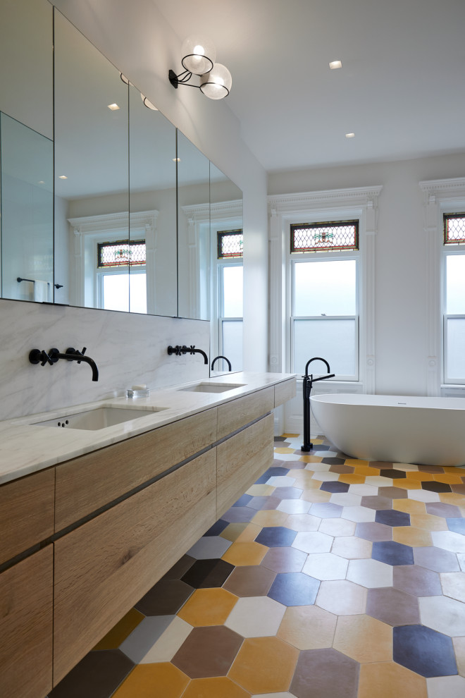 Photo of a mid-sized contemporary master bathroom in New York with flat-panel cabinets, light wood cabinets, a freestanding tub, white tile, marble, white walls, cement tiles, an undermount sink, marble benchtops, yellow floor and white benchtops.