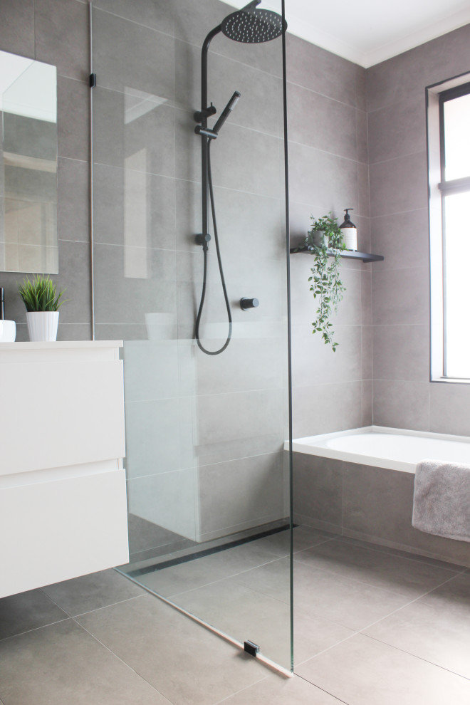 Photo of a mid-sized modern kids wet room bathroom in Perth with flat-panel cabinets, white cabinets, a drop-in tub, a one-piece toilet, gray tile, porcelain tile, grey walls, porcelain floors, a vessel sink, engineered quartz benchtops, grey floor, an open shower, white benchtops, a single vanity and a floating vanity.