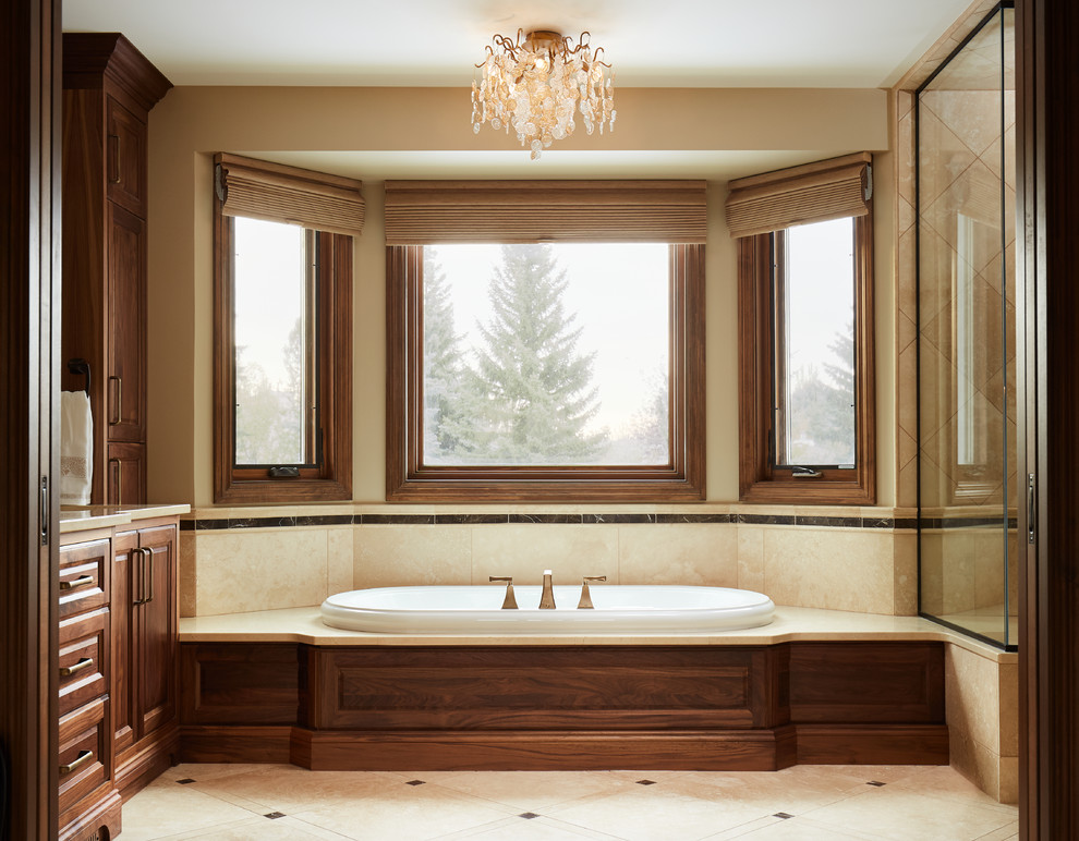 Large traditional master bathroom in Edmonton with raised-panel cabinets, dark wood cabinets, a drop-in tub, a corner shower, beige tile, travertine, beige walls, travertine floors, an undermount sink, marble benchtops, beige floor and a hinged shower door.