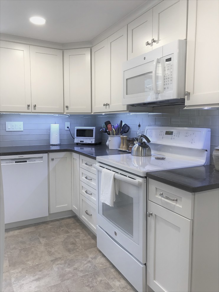 Photo of a mid-sized transitional l-shaped eat-in kitchen in Bridgeport with a double-bowl sink, shaker cabinets, white cabinets, quartz benchtops, beige splashback, glass tile splashback, white appliances, linoleum floors, no island, brown floor and brown benchtop.