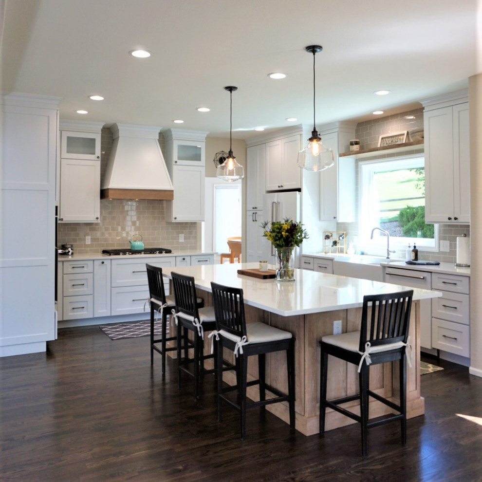Photo of a large transitional l-shaped open plan kitchen in Denver with a farmhouse sink, shaker cabinets, white cabinets, quartz benchtops, glass tile splashback, white appliances, with island and white benchtop.