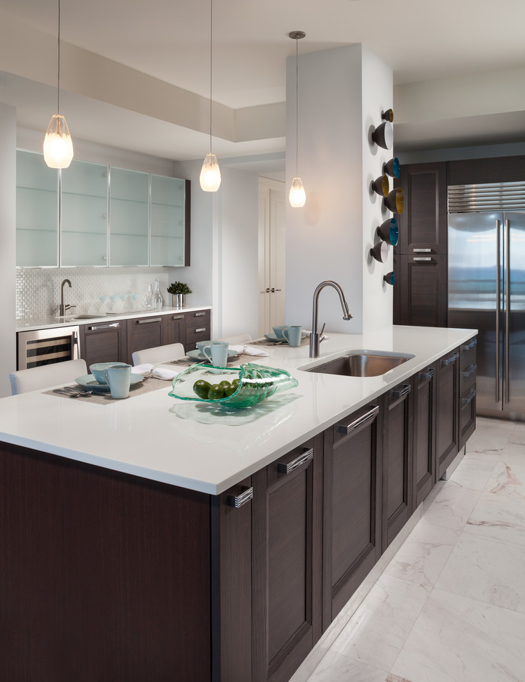 Mid-sized contemporary l-shaped open plan kitchen in Miami with a single-bowl sink, recessed-panel cabinets, brown cabinets, glass benchtops, white splashback, mosaic tile splashback, stainless steel appliances, marble floors, with island, white floor and white benchtop.