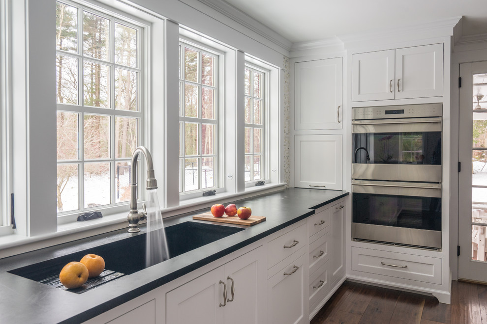 Mid-sized transitional l-shaped separate kitchen in Boston with an integrated sink, recessed-panel cabinets, white cabinets, soapstone benchtops, multi-coloured splashback, porcelain splashback, stainless steel appliances, dark hardwood floors, with island and brown floor.