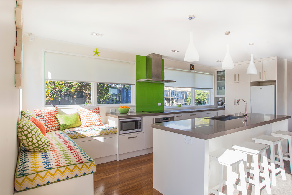 Inspiration for a small contemporary galley open plan kitchen in Auckland with an undermount sink, flat-panel cabinets, white cabinets, quartz benchtops, green splashback, glass sheet splashback, white appliances, dark hardwood floors and with island.