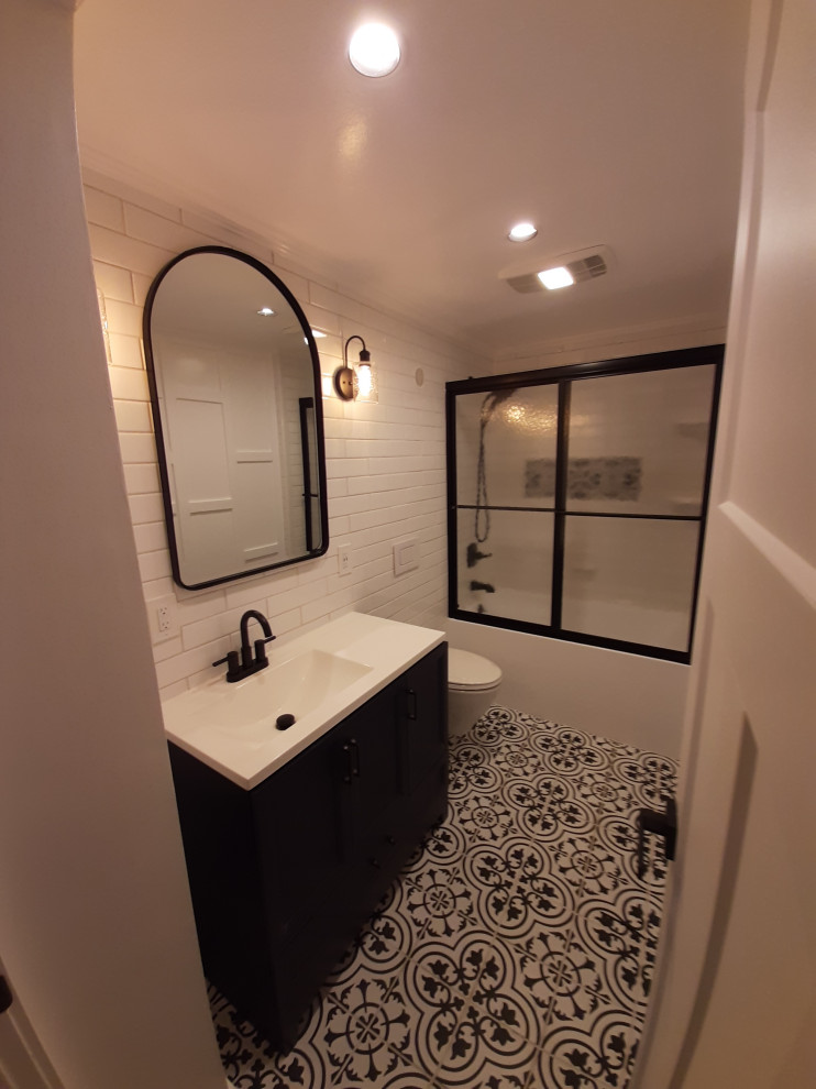 This is an example of a medium sized classic shower room bathroom in Detroit with shaker cabinets, blue cabinets, an alcove bath, a shower/bath combination, a wall mounted toilet, white tiles, porcelain tiles, white walls, porcelain flooring, engineered stone worktops, multi-coloured floors, a sliding door, white worktops, a single sink, a freestanding vanity unit and wainscoting.