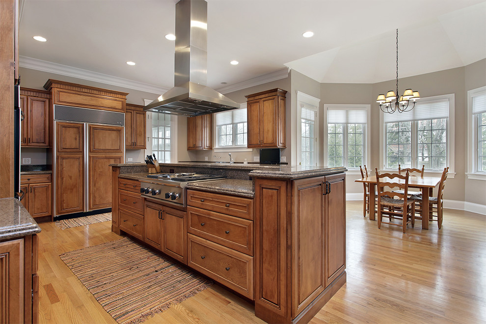 Example of a mid-sized transitional u-shaped medium tone wood floor and brown floor eat-in kitchen design in Edmonton with an undermount sink, shaker cabinets, brown cabinets, granite countertops, stainless steel appliances, an island and brown countertops