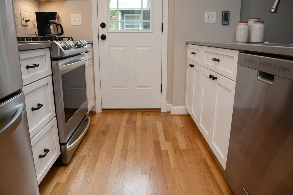 Photo of a small traditional l-shaped separate kitchen in DC Metro with a double-bowl sink, recessed-panel cabinets, white cabinets, quartz benchtops, white splashback, stainless steel appliances, light hardwood floors, with island and brown floor.