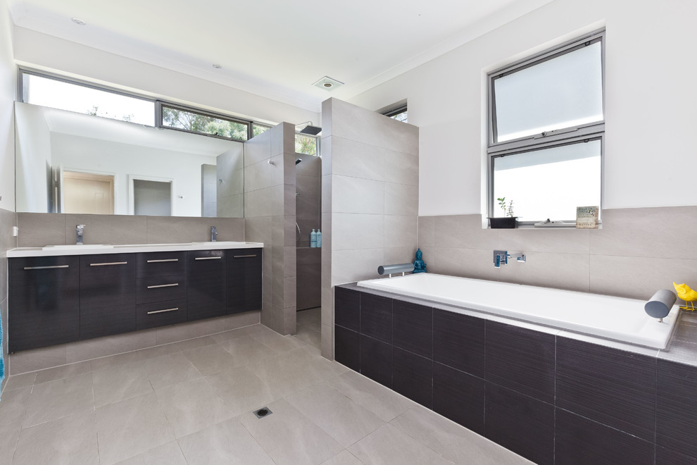 Inspiration for a mid-sized contemporary master bathroom in Perth with dark wood cabinets, a drop-in tub, an alcove shower, gray tile, porcelain tile, grey walls, porcelain floors, a drop-in sink, solid surface benchtops, flat-panel cabinets, grey floor, an open shower and white benchtops.