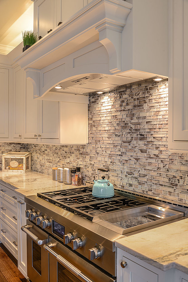 Inspiration for a large transitional l-shaped open plan kitchen in Tampa with a farmhouse sink, beaded inset cabinets, white cabinets, quartzite benchtops, metallic splashback, glass tile splashback, stainless steel appliances, light hardwood floors and with island.