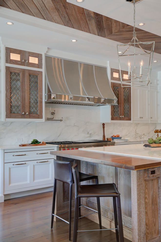 Inspiration for a large transitional u-shaped eat-in kitchen in New York with a farmhouse sink, flat-panel cabinets, white cabinets, marble benchtops, white splashback, marble splashback, stainless steel appliances, dark hardwood floors, with island, brown floor, white benchtop and wood.