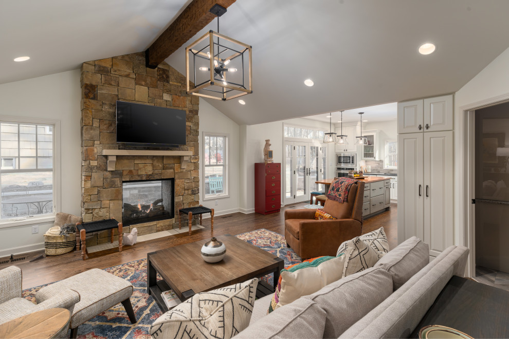 Design ideas for a large open plan games room in Kansas City with white walls, medium hardwood flooring, a two-sided fireplace, a stone fireplace surround, a wall mounted tv and a vaulted ceiling.